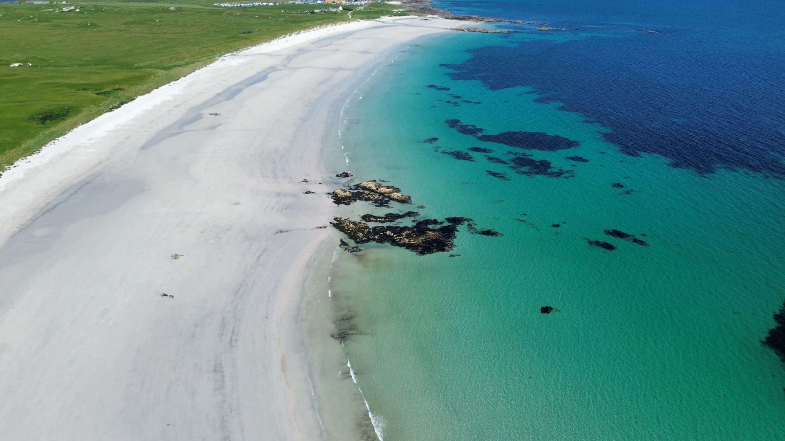 Beautiful coastal landscape with pristine white beach, clear blue sea, and rocky outcrops.