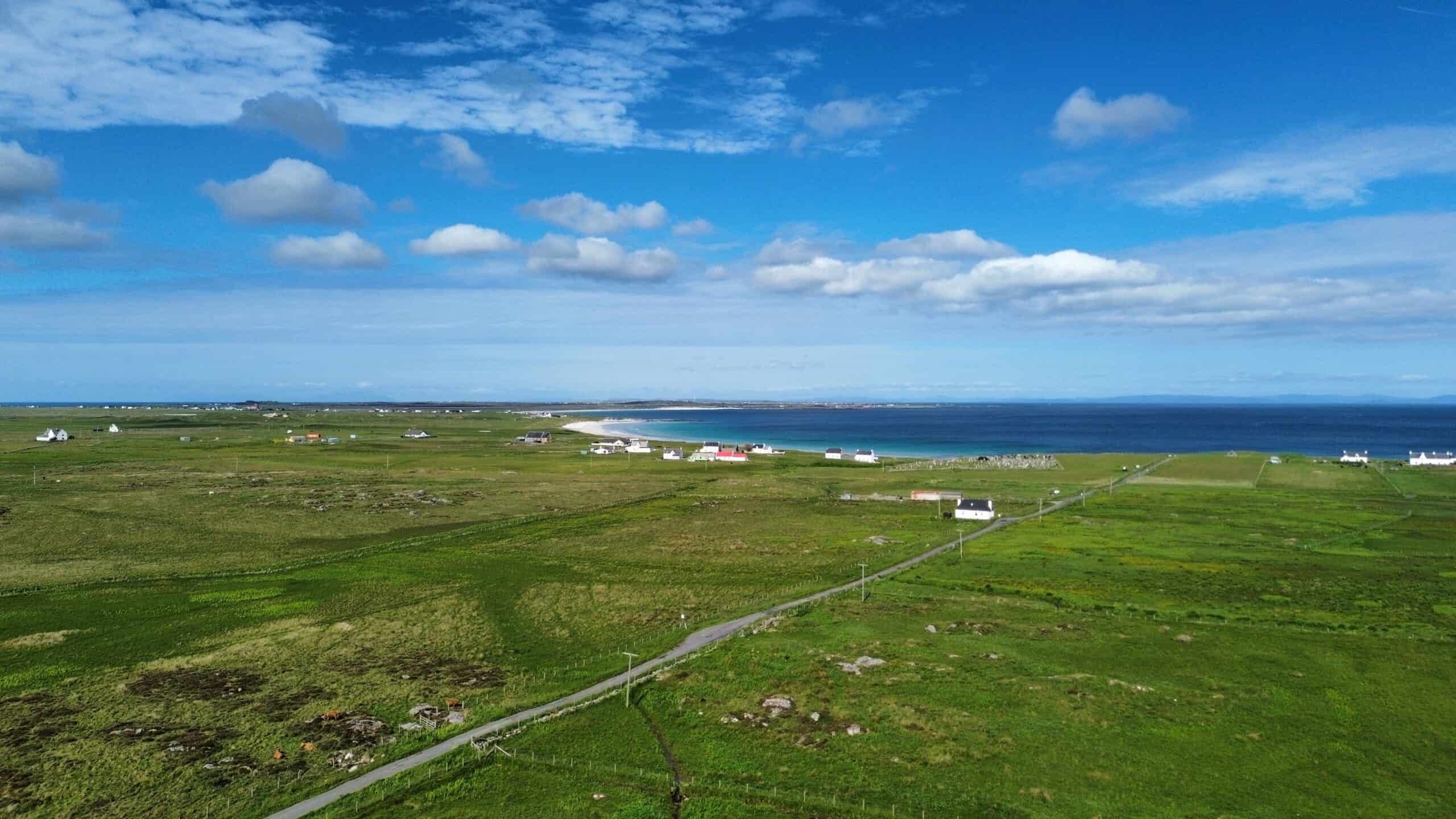 Scenic coastal landscape with green fields, houses, and blue sky in the background.
