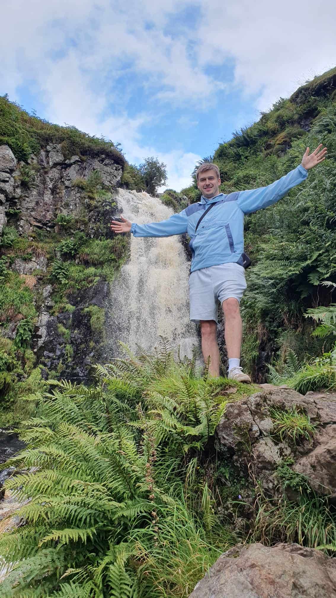 Lush forest waterfall scene with a smiling man in outdoor hiking gear.