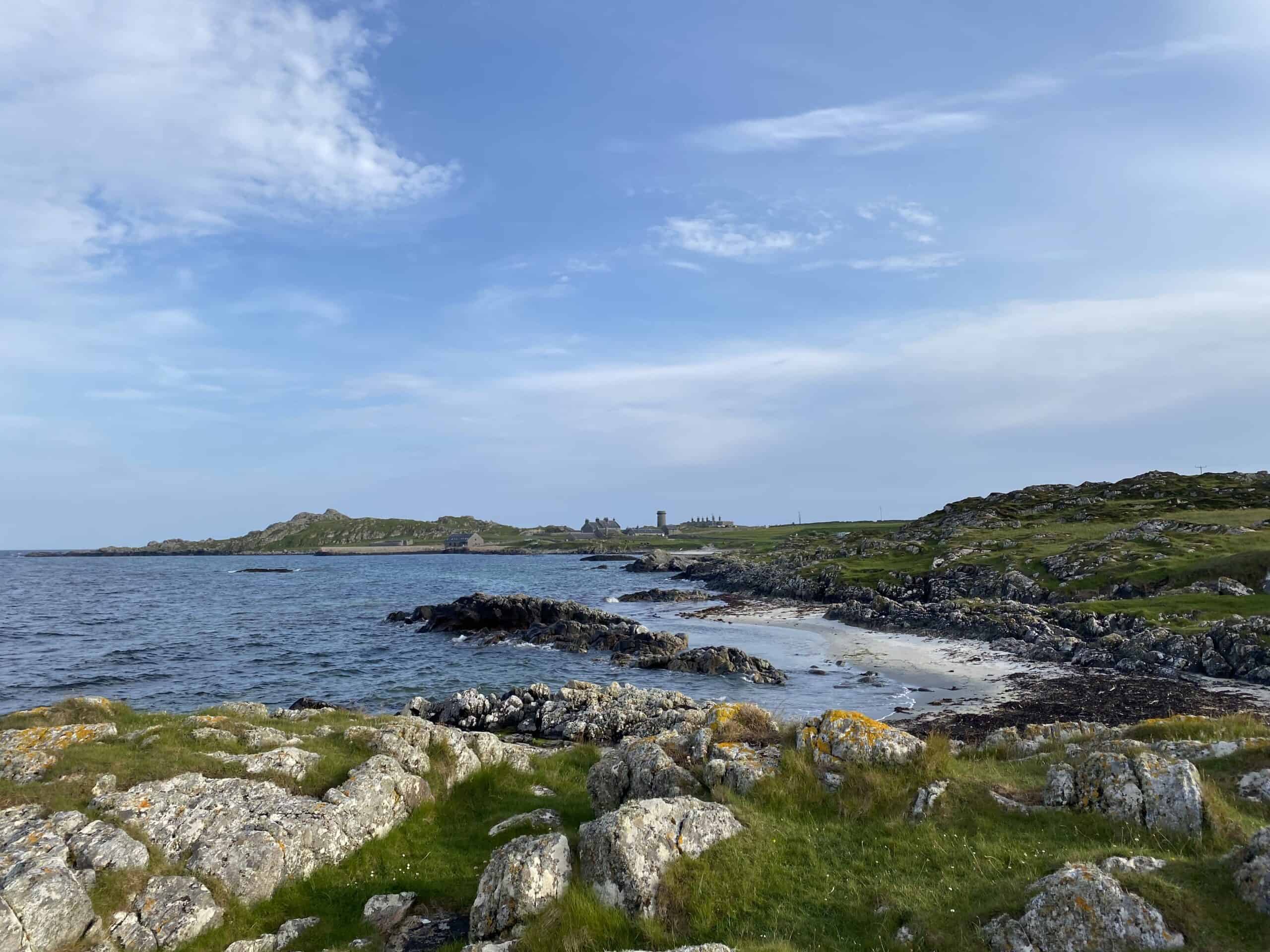 Wild coastal landscape with rocky shoreline and green hills in the distance, Scotland.